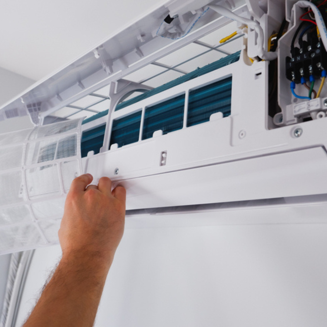 Technicien procédant au retrait et au nettoyage du filtre d'une unité de climatisation murale lors d'une intervention de maintenance.